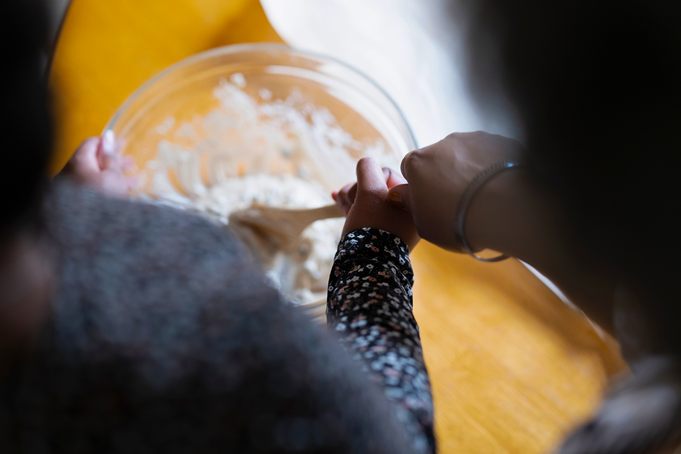 adult and child holding wooden spoon mixing dough in a bowl