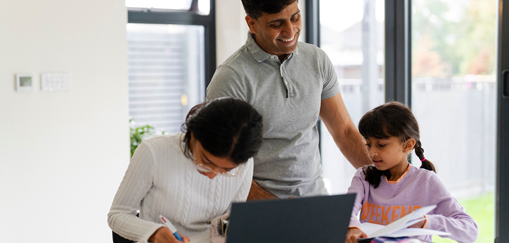 adult man helping a child and teenager to study. They are studying at a laptop in a white room