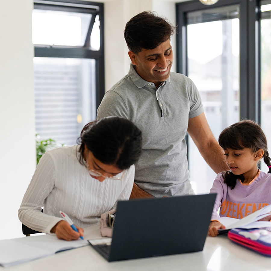 adult man helping a child and teenager to study. They are studying at a laptop in a white room