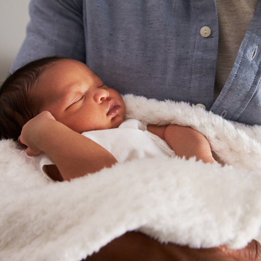 Young baby being held by a woman as they sleep wrapped up in a white fluffy blanket.