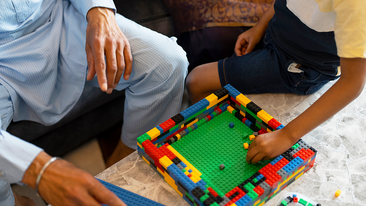 Child and adult playing with lego on a table.