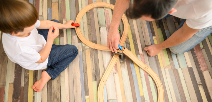 Aerial shot of a young boy and adult man playing with toy cars on a wooden track